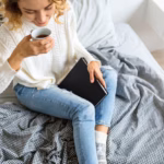 view-from-woman-sitting-bed-morning-drinking-coffee-cup-holding-book-wearing-jeans_285396-1924